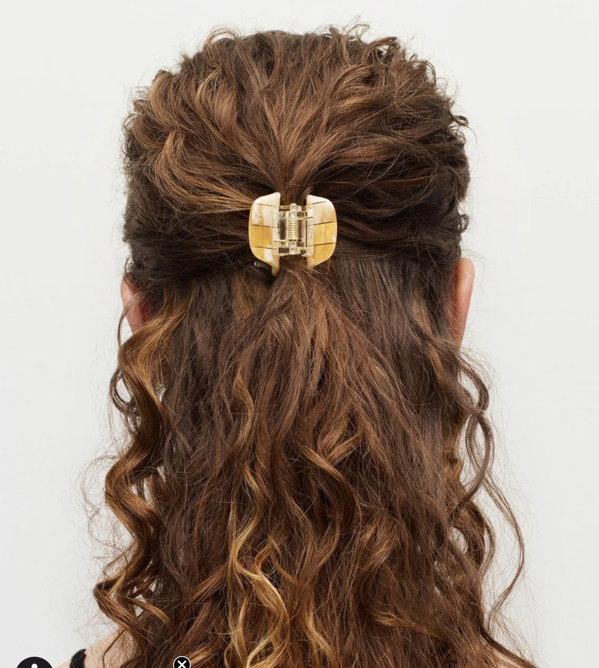 Close-up of a person with wavy hair wearing a gold hair clip on a white background