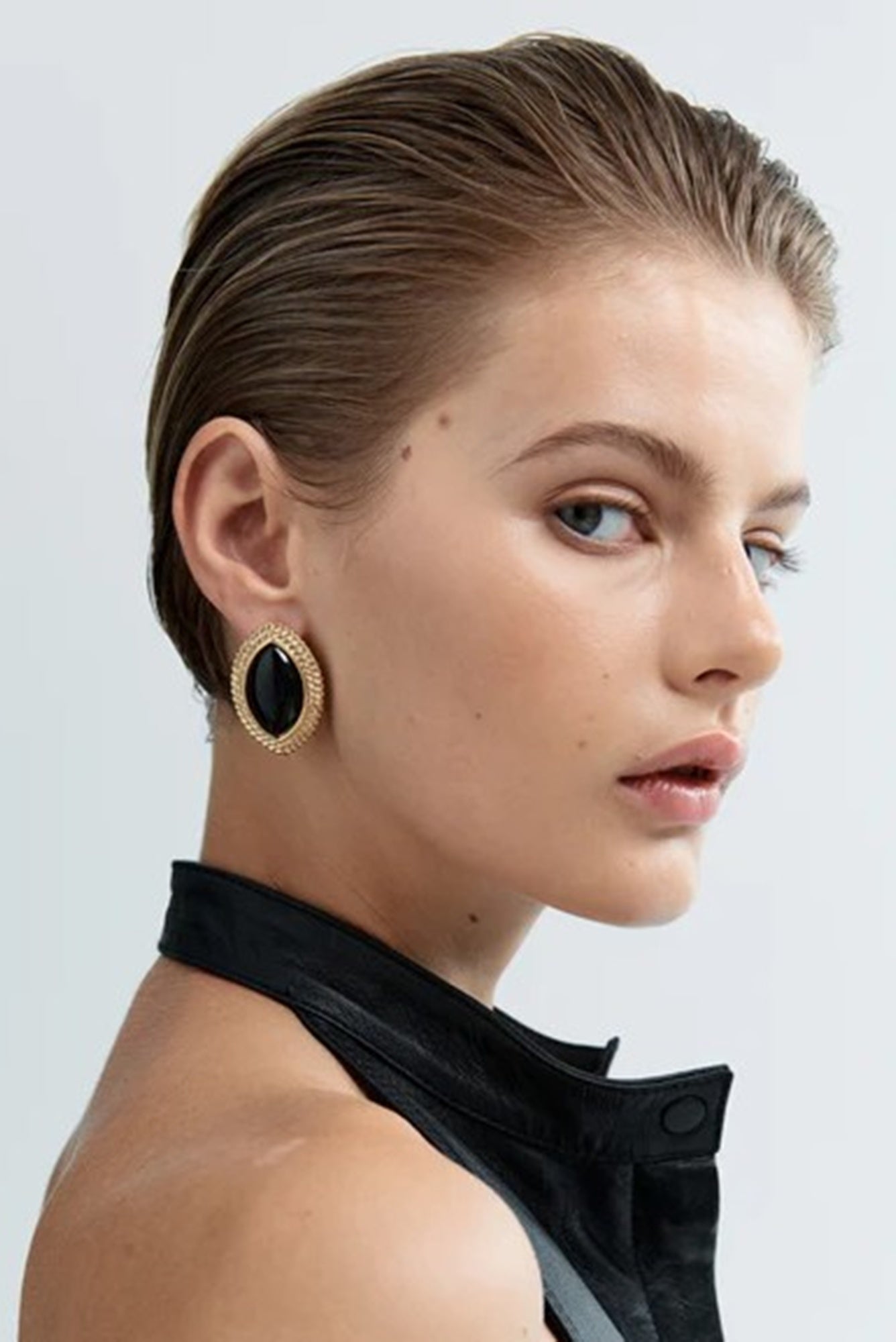 Woman wearing gold hoop earrings with black stones on a plain background