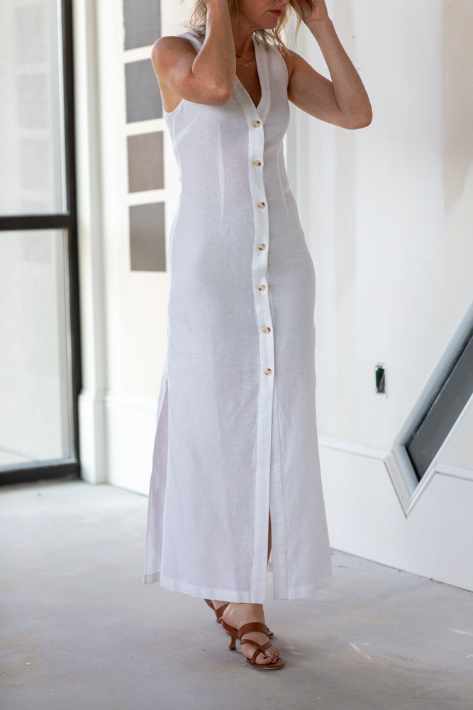 Woman wearing a long white dress with buttons in a minimal indoor setting