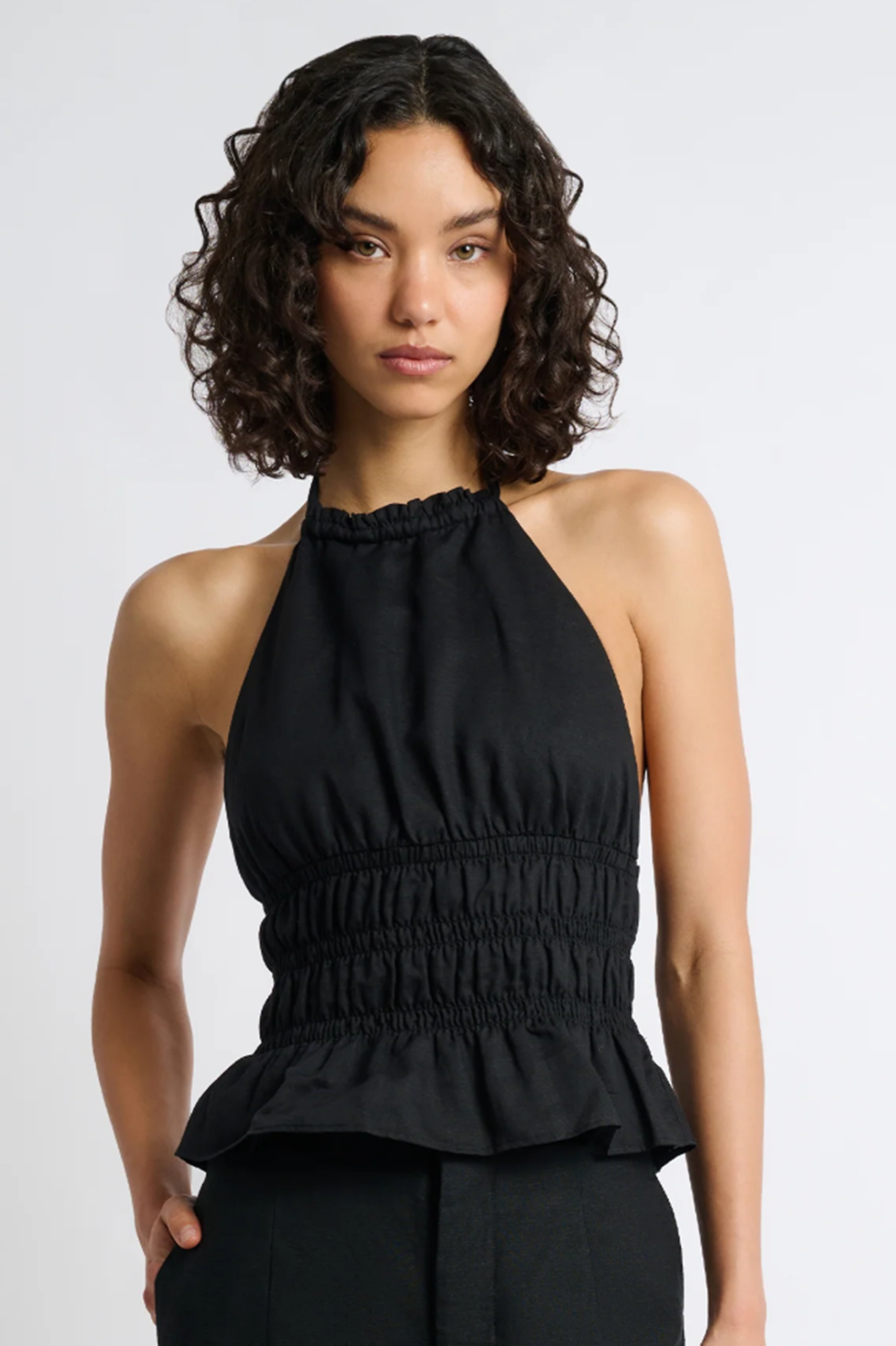 Woman wearing a black halter top with smocked details on a white background