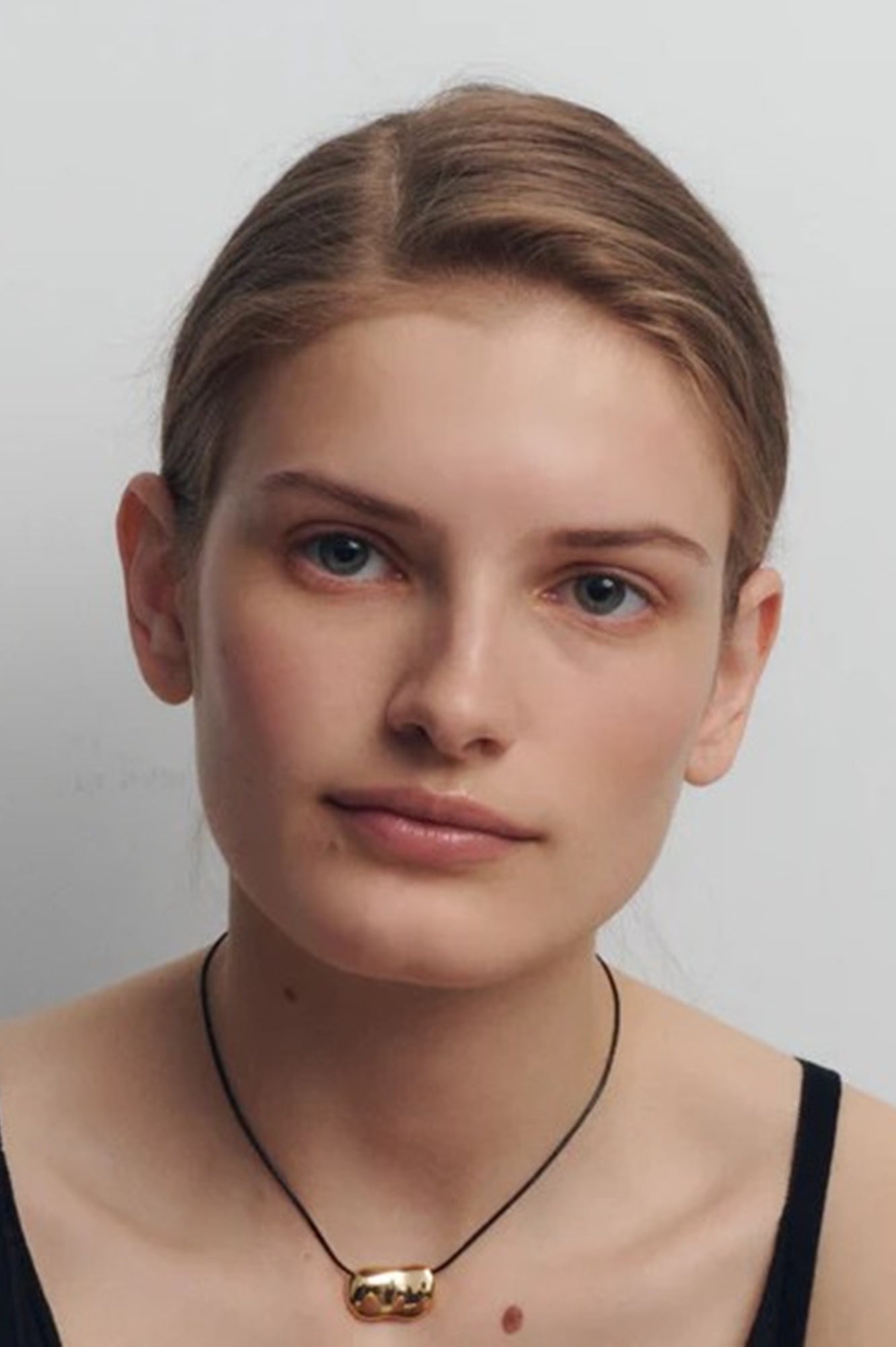 Woman wearing a necklace with a gold pendant against a plain background