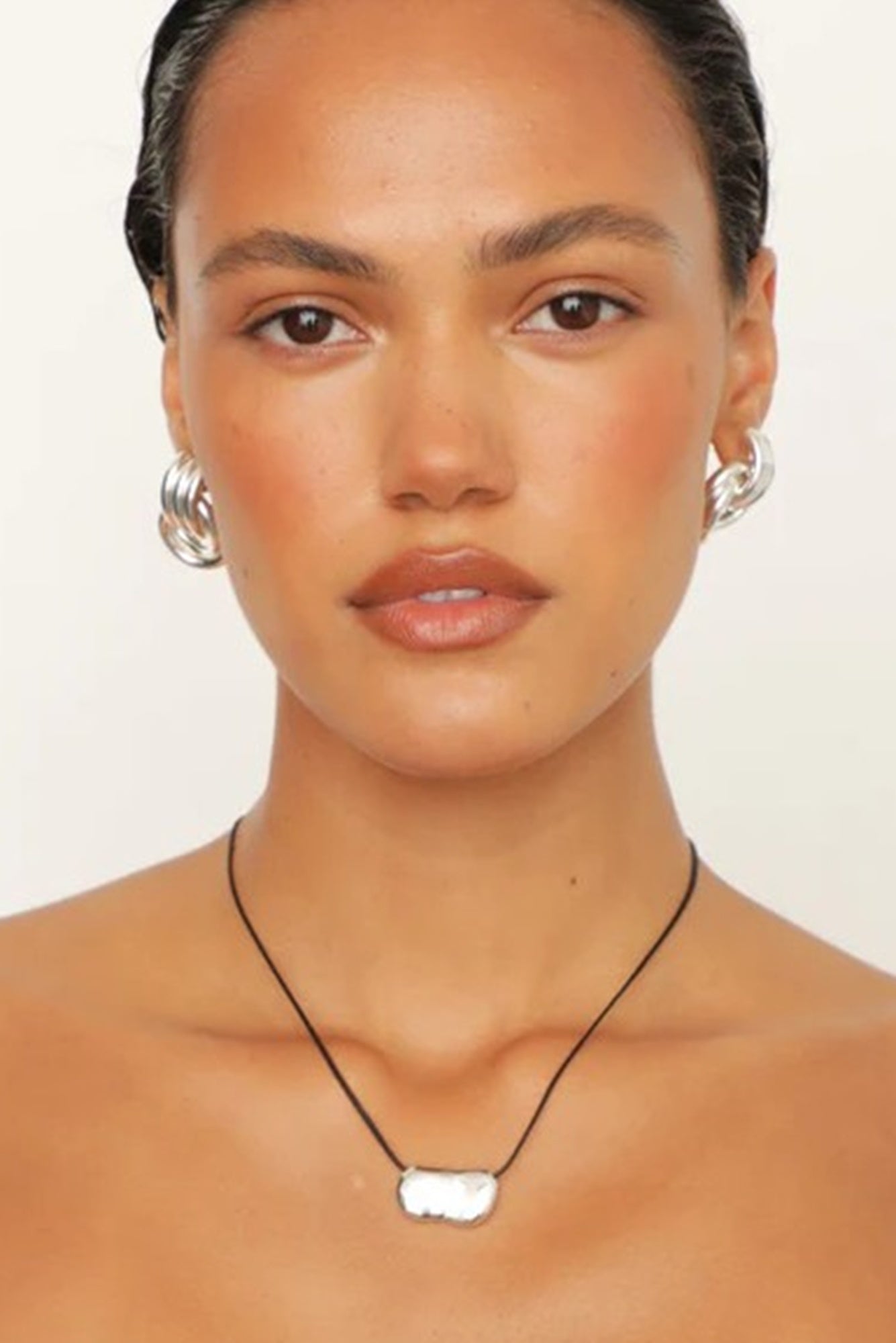 Woman wearing a necklace with a white pendant against a plain background