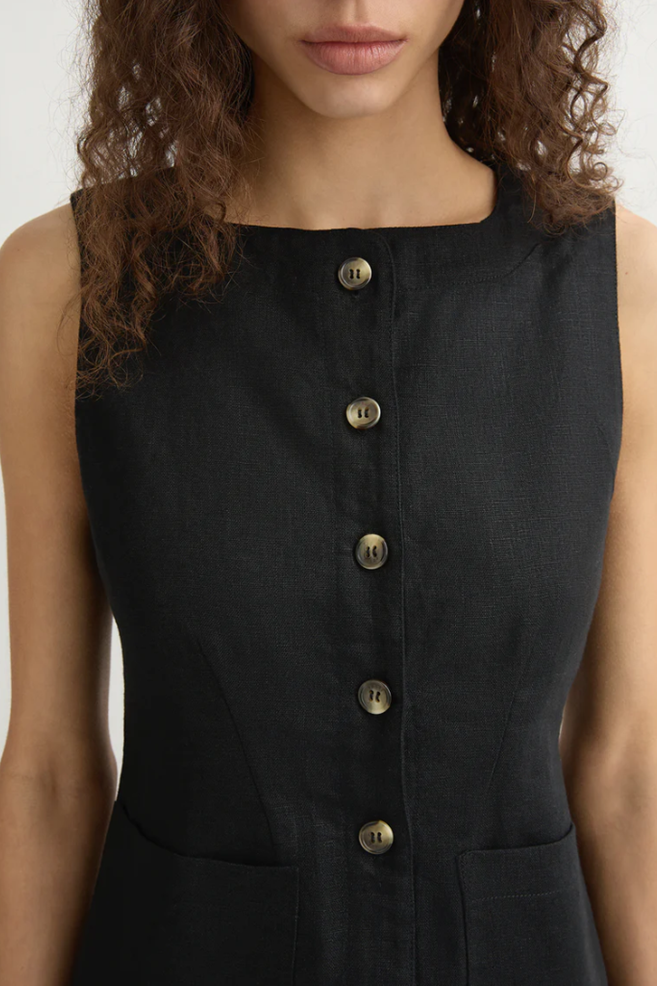 Black sleeveless dress with gold buttons worn by a person
