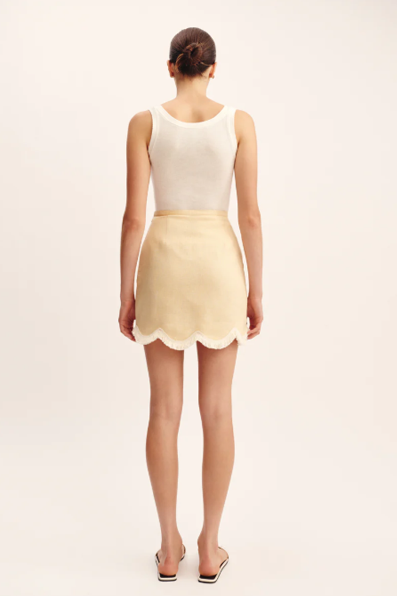 Woman wearing a white top and yellow skirt on a beige background