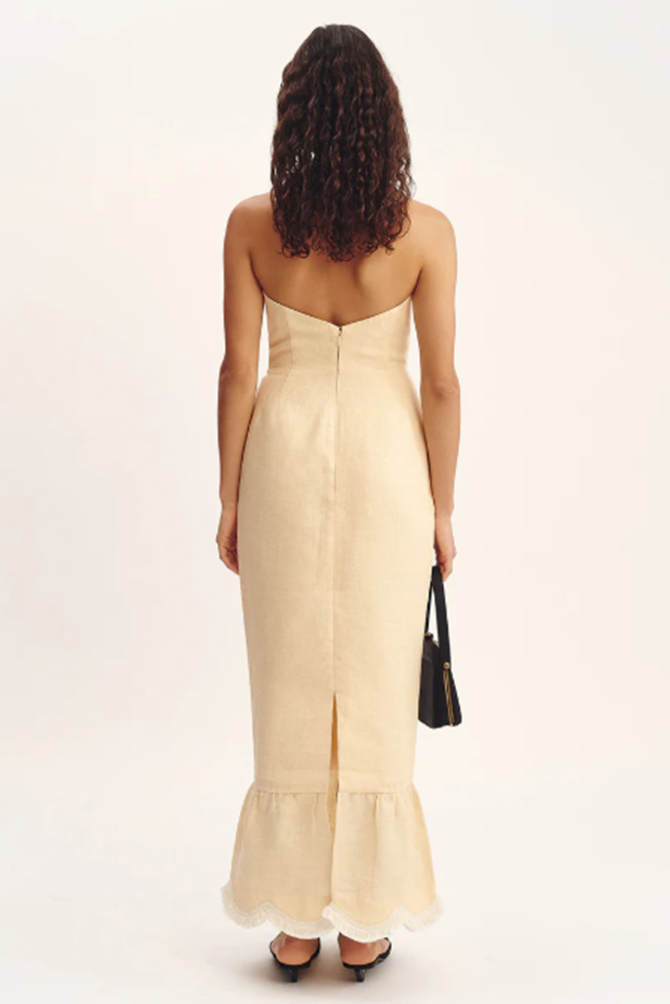 Woman wearing a beige strapless dress with a black handbag on a white background