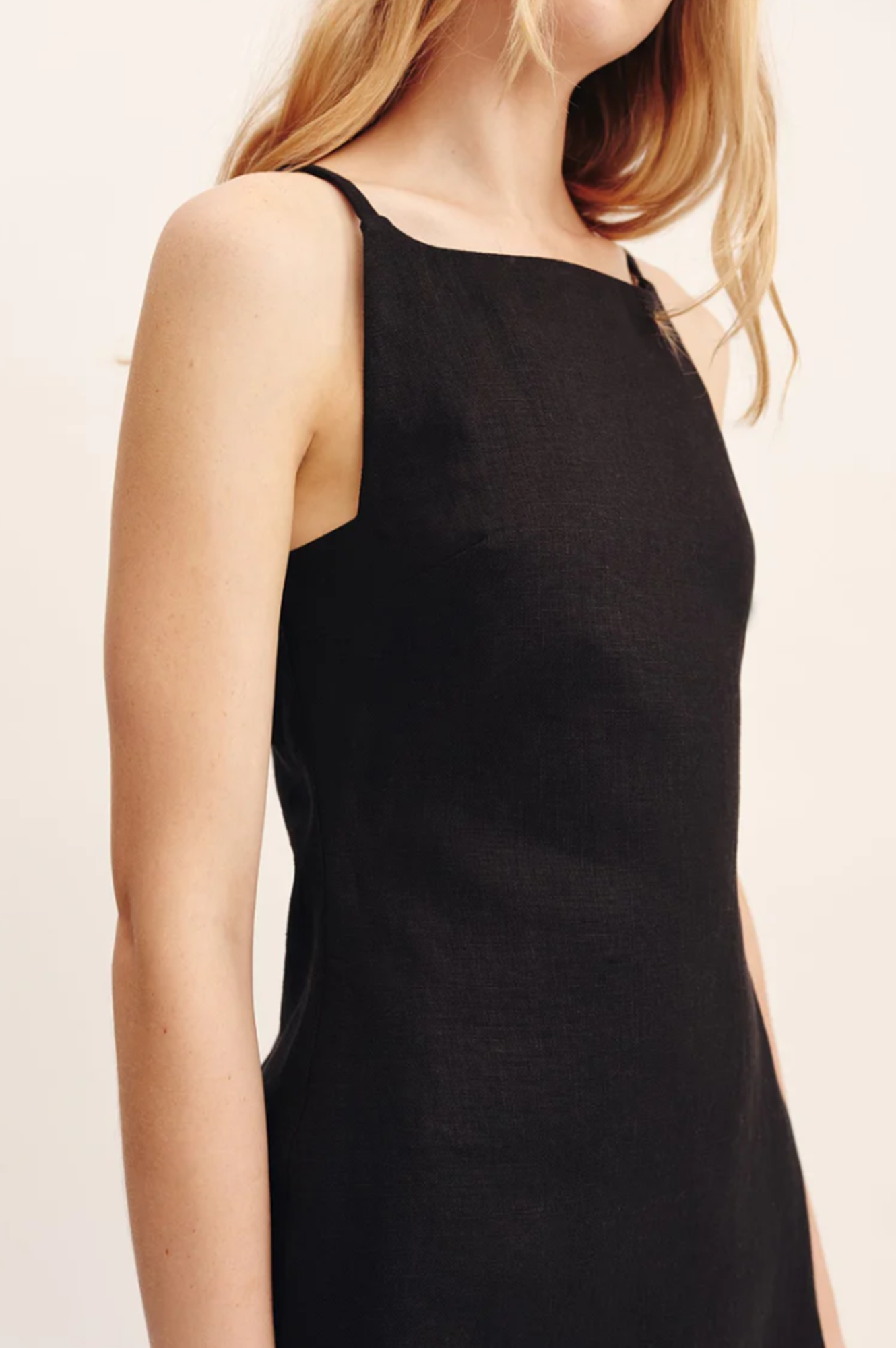 Black sleeveless dress worn by a person on a light pink background
