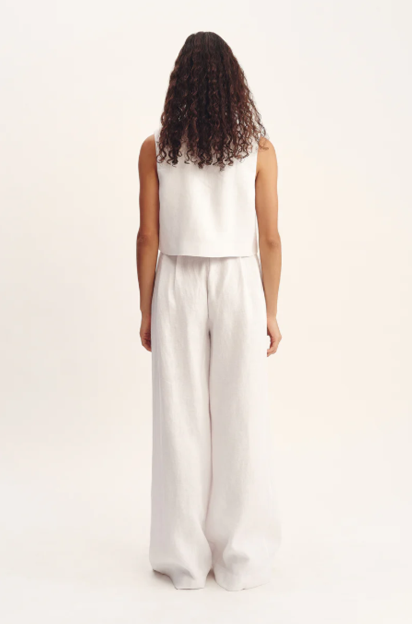 Person wearing a white sleeveless top and wide-leg pants on a plain background