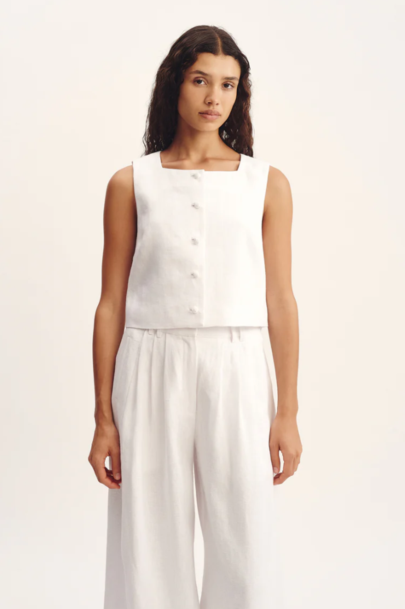 Woman wearing a white sleeveless top and pants on a plain background