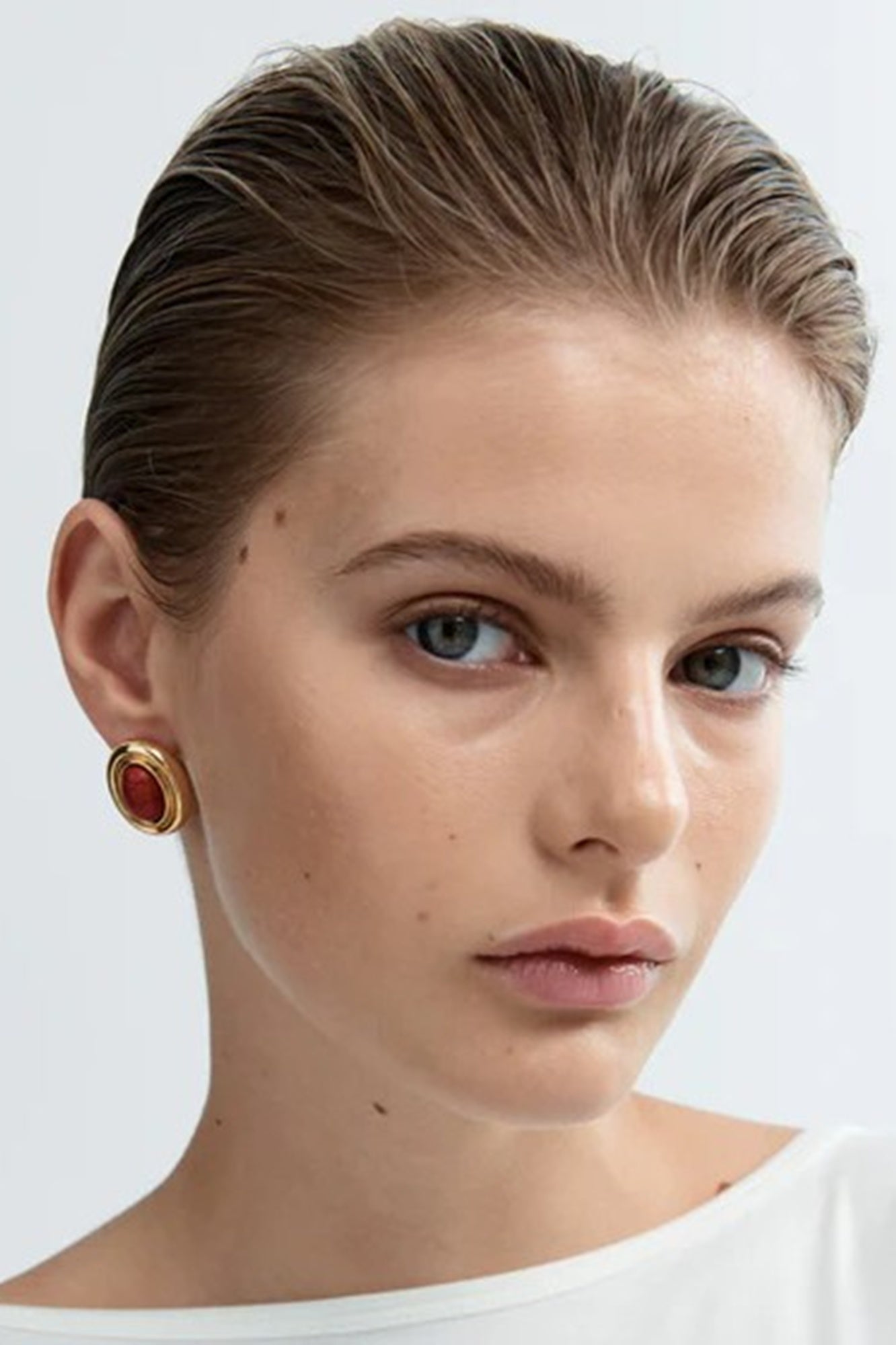 Close-up of a woman wearing gold earrings with red stones on a white background