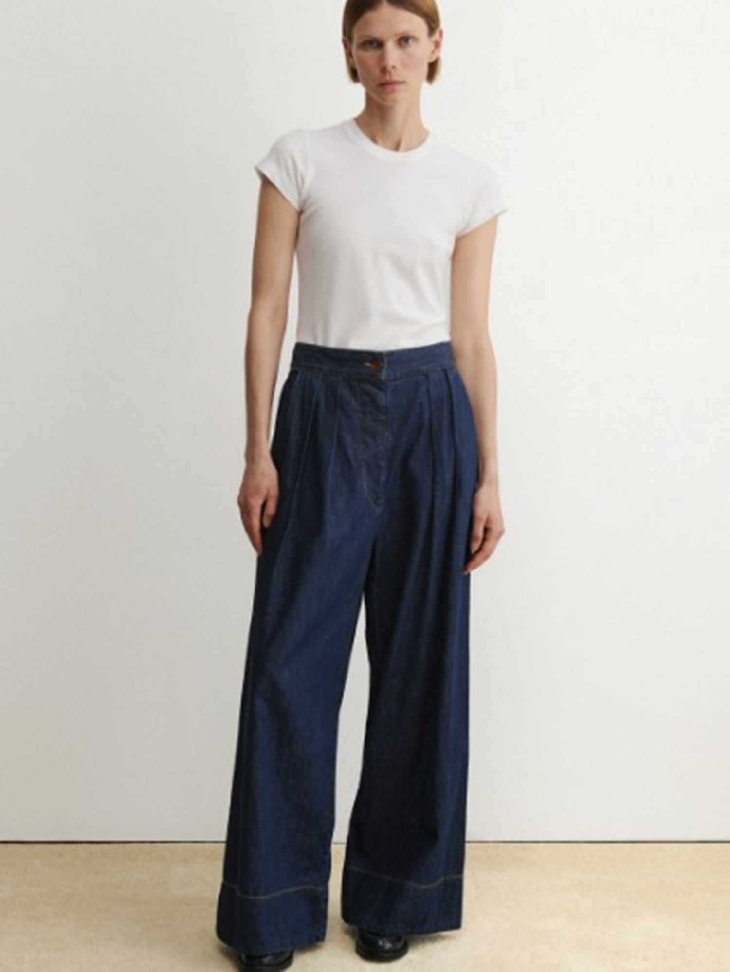Person wearing a white t-shirt and blue wide-leg pants on a plain background