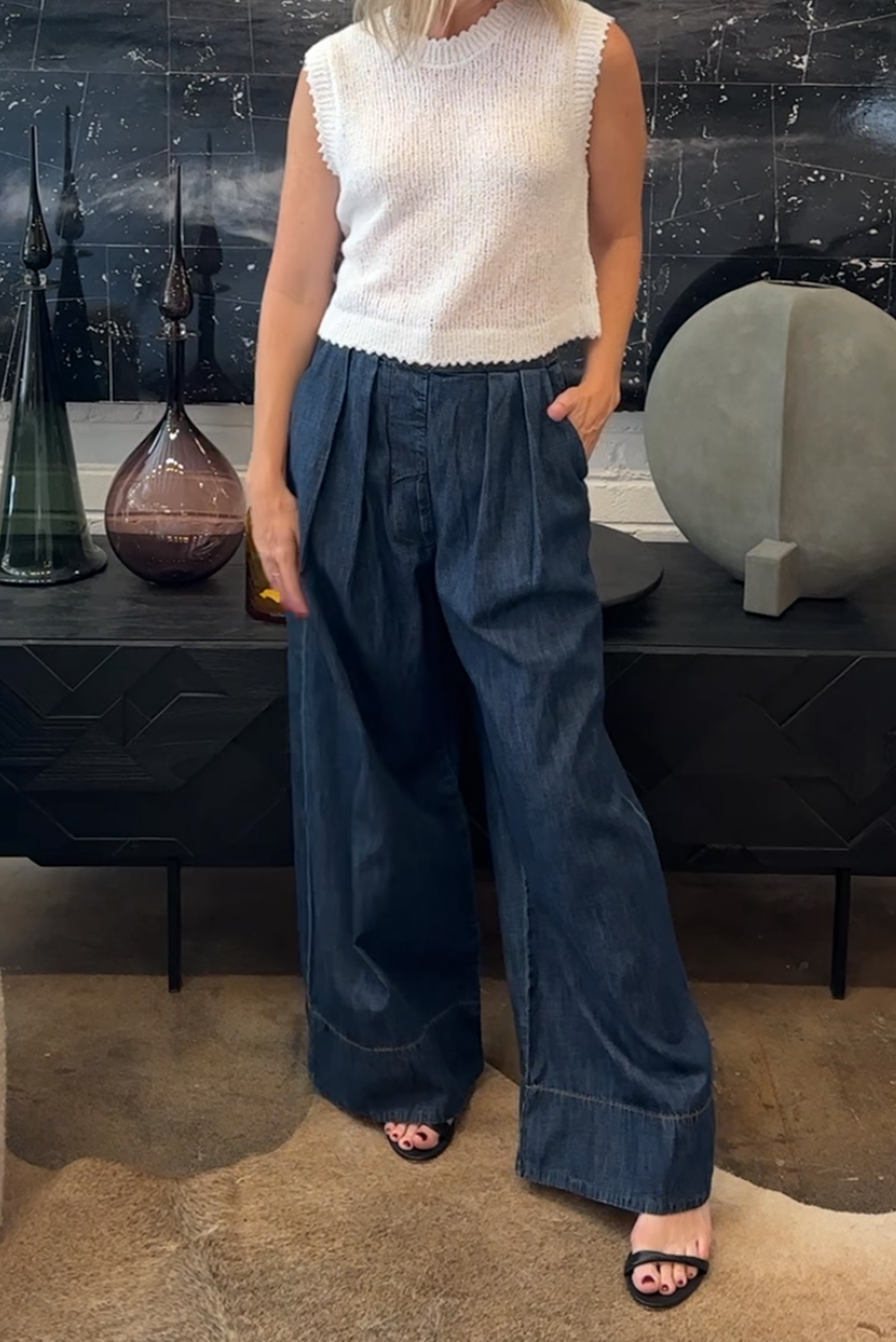 Person wearing a white sleeveless top and blue wide-leg pants in an indoor setting.