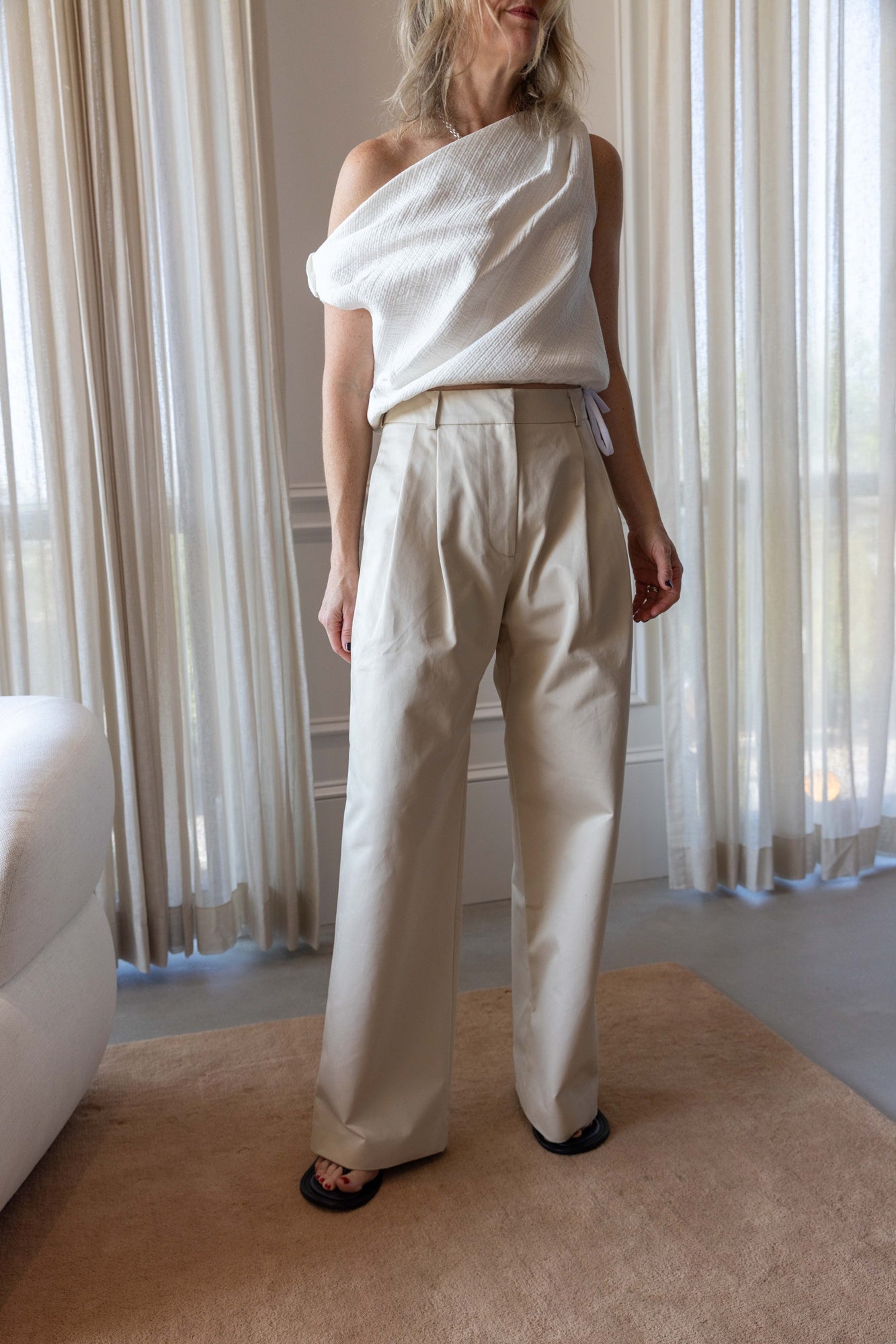 Woman wearing the Rachel Comey Farfalla Top in white and the alfie tailored pant standing in front of white curtains