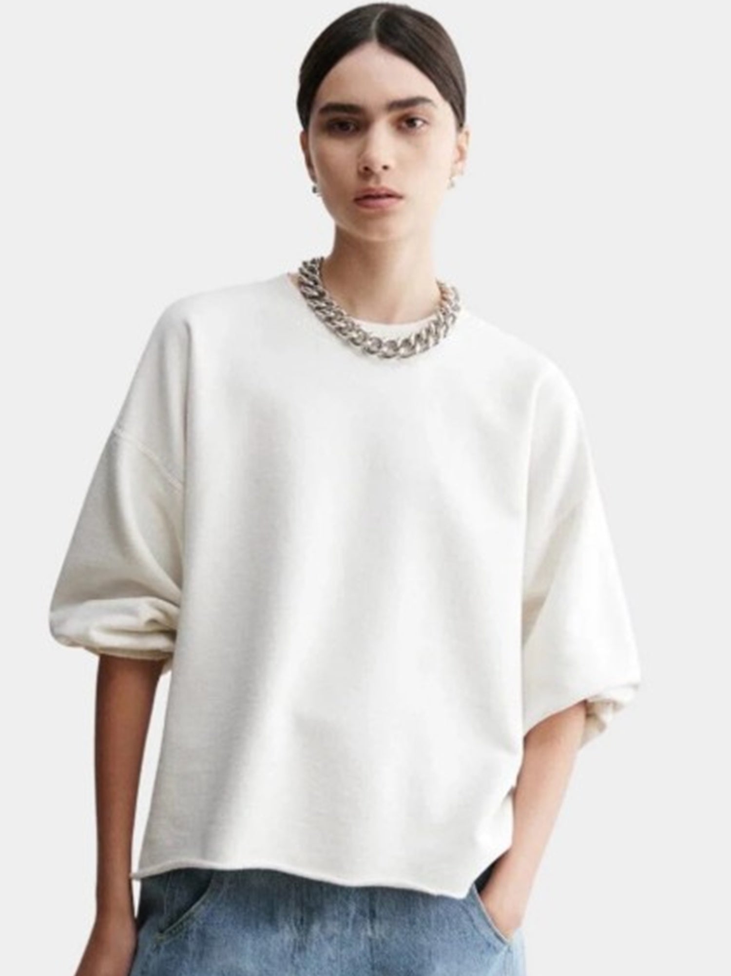 Person wearing a white oversized sweater and blue jeans on a plain background