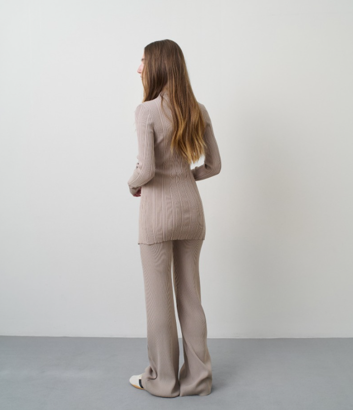 Woman wearing a beige ribbed sweater and pants set against a plain background