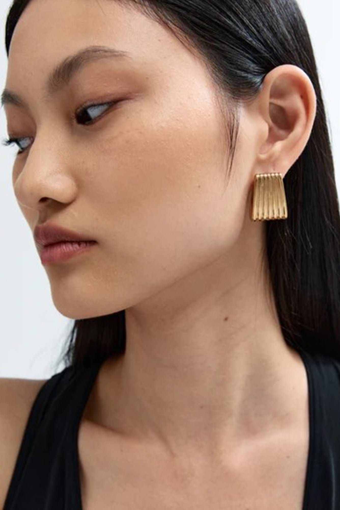 Close-up of a person wearing gold earrings with a neutral background