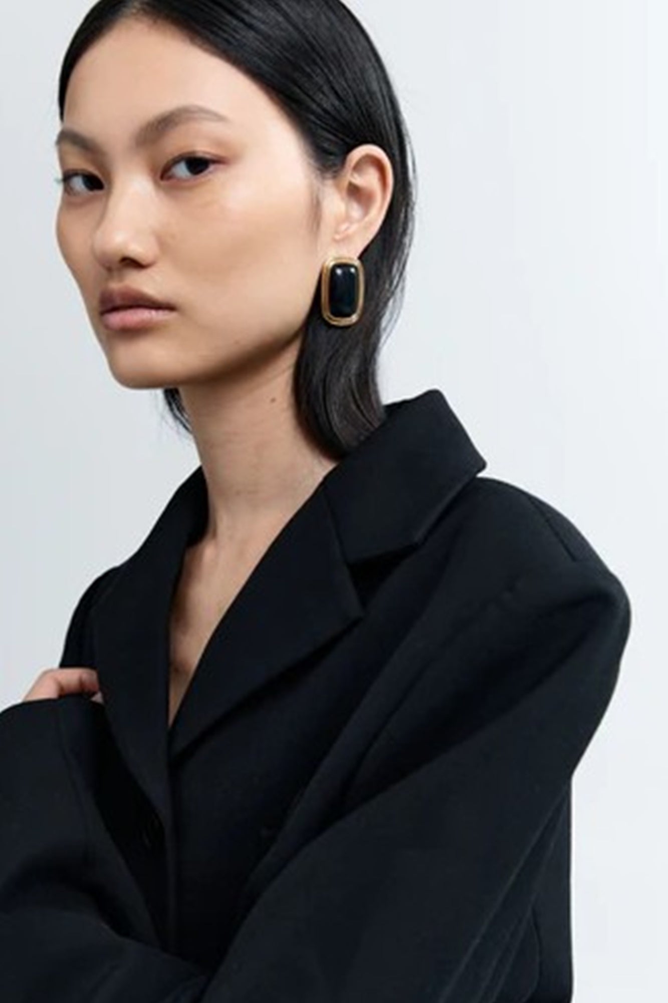 Woman wearing a black coat and earrings on a light gray background