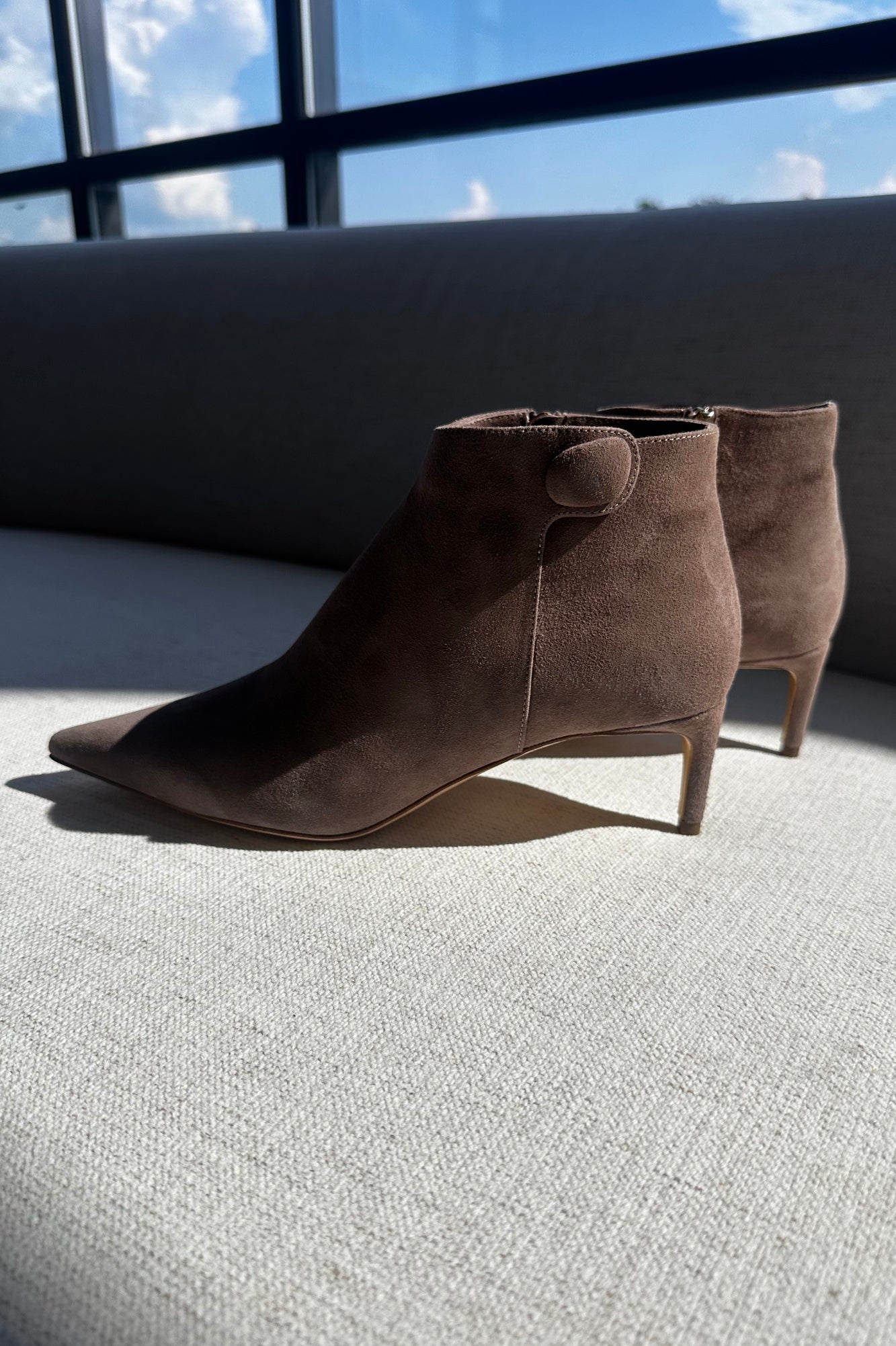 Pair of brown suede ankle boots on a light gray surface with a window in the background.