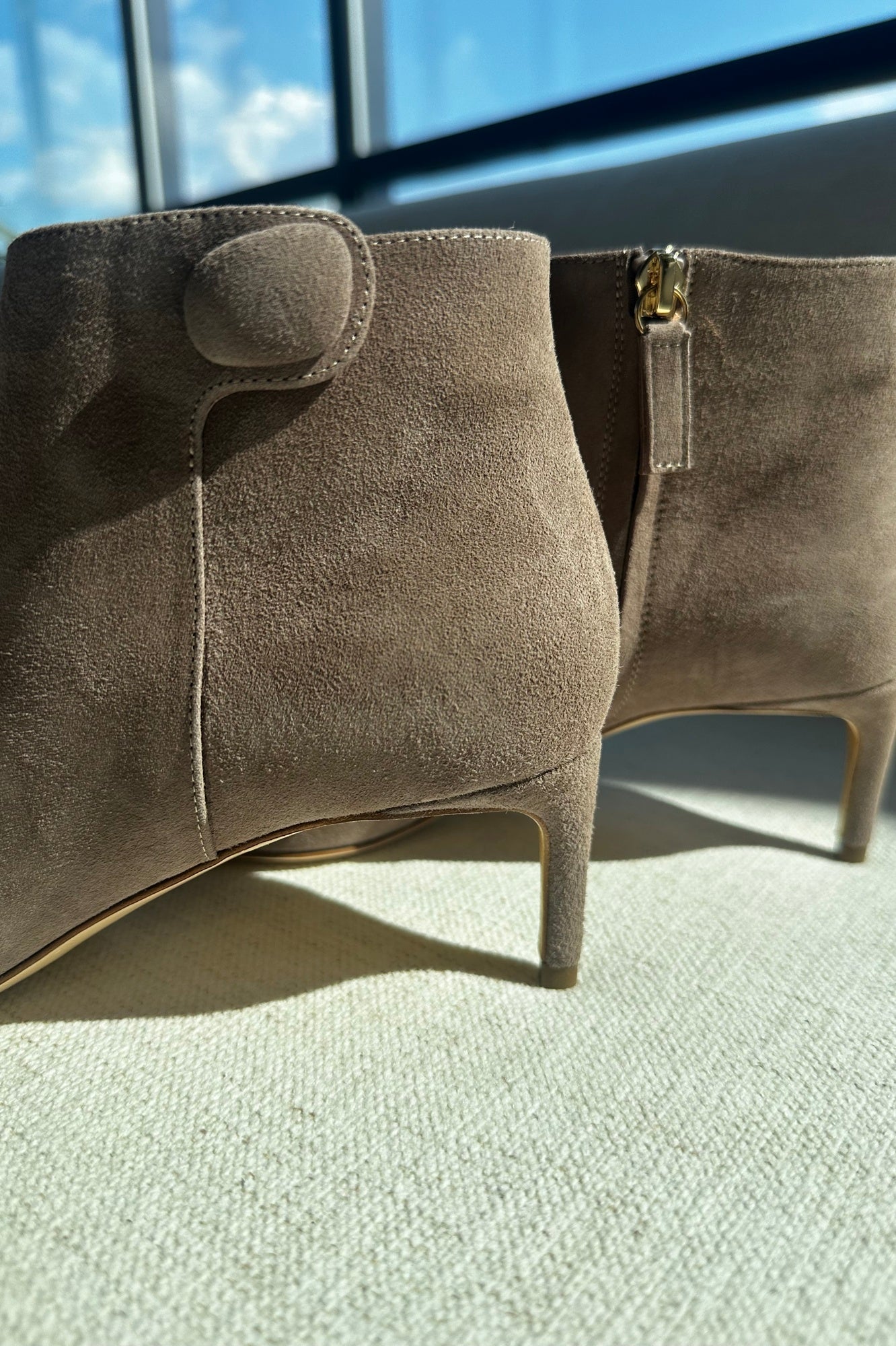 Pair of brown suede ankle boots on a light green surface with a blurred background