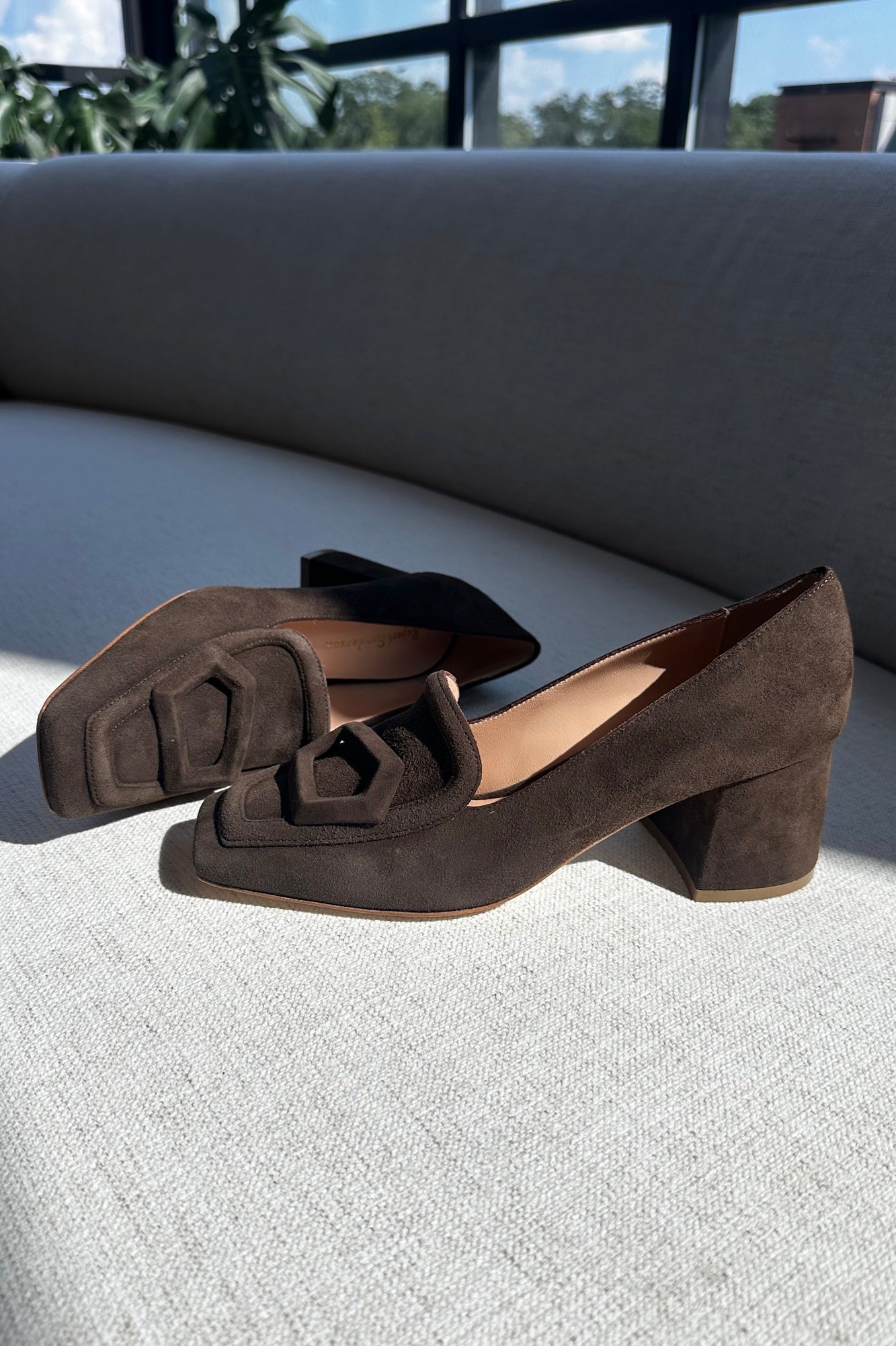 Brown suede shoes on a light gray surface with a blurred outdoor background
