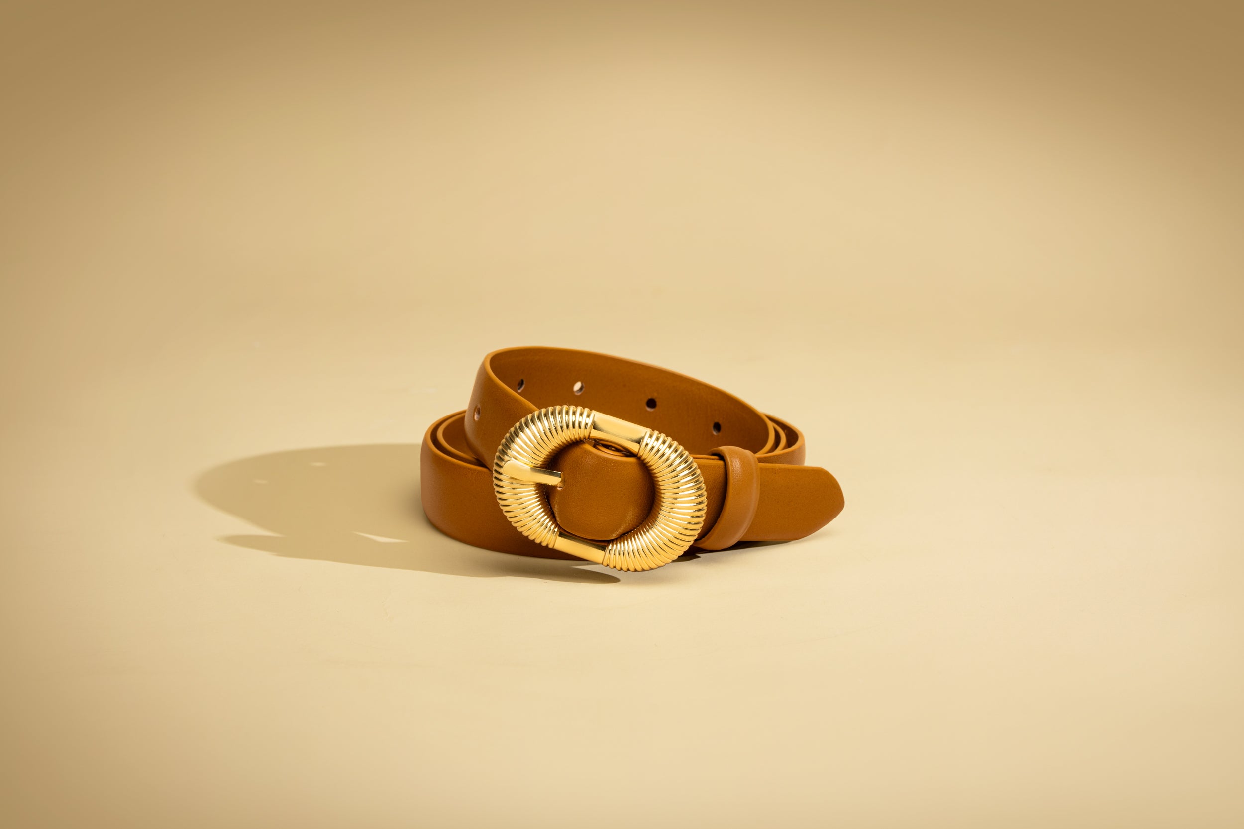 Brown belt with a gold buckle on a beige background