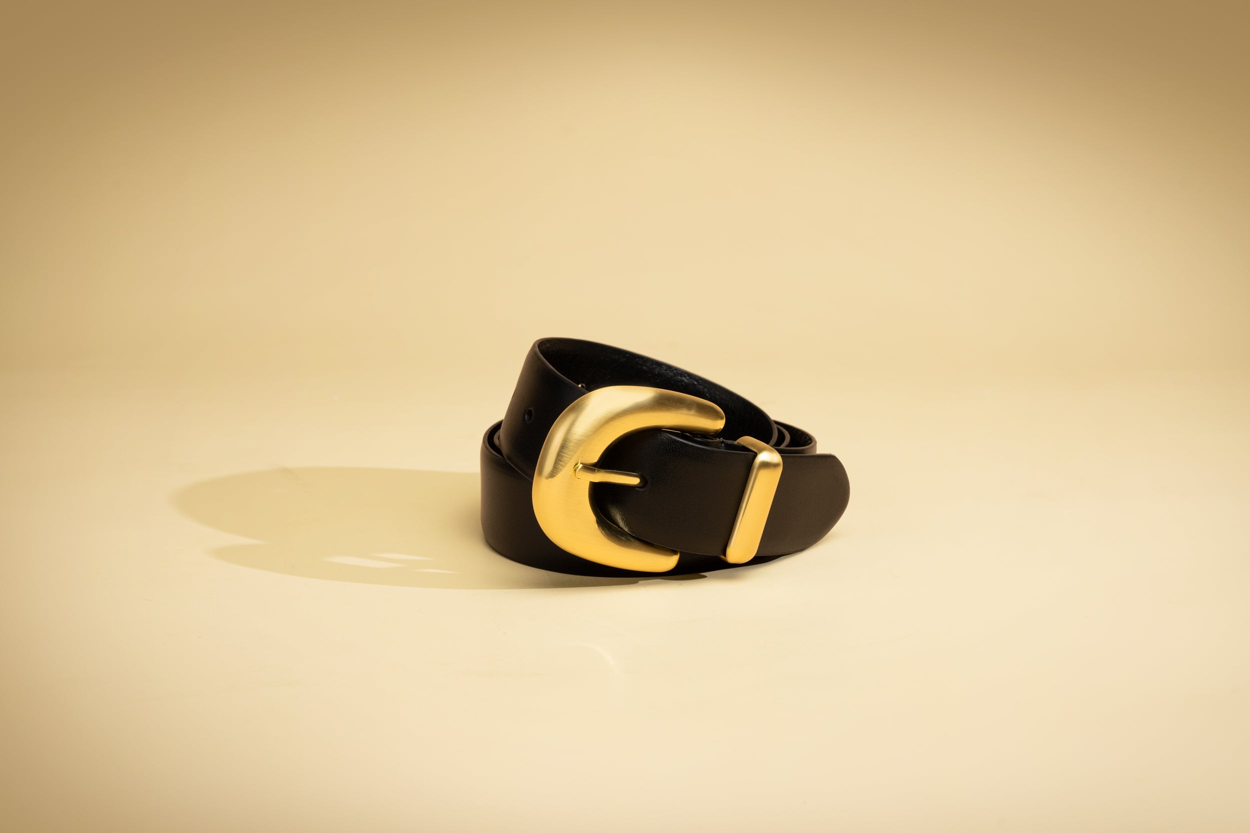 Black belt with a gold buckle on a beige background