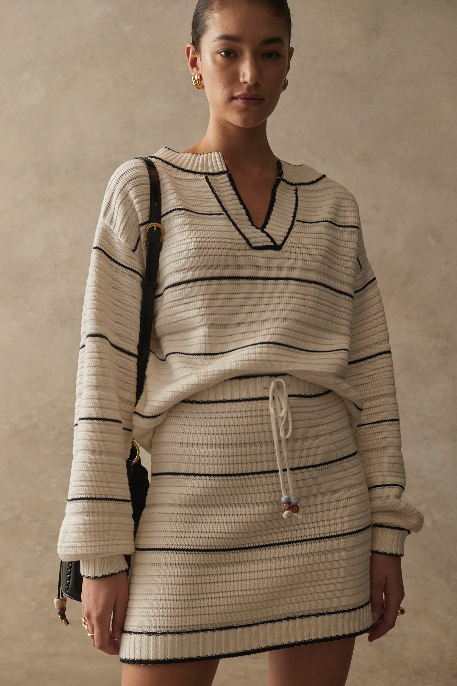 Woman wearing a striped sweater and skirt set against a neutral background