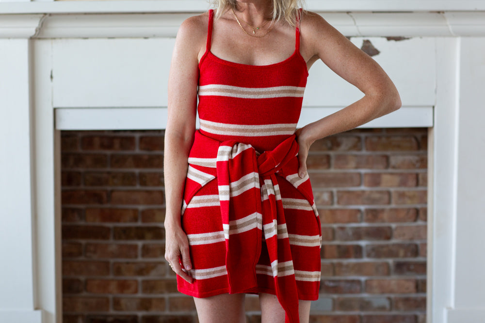 Woman wearing a red and white striped dress against a brick wall.