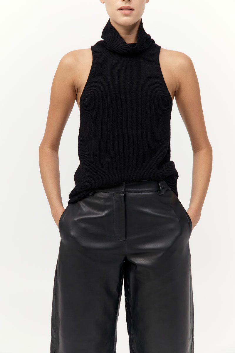 Person wearing a black sleeveless top and leather pants on a white background