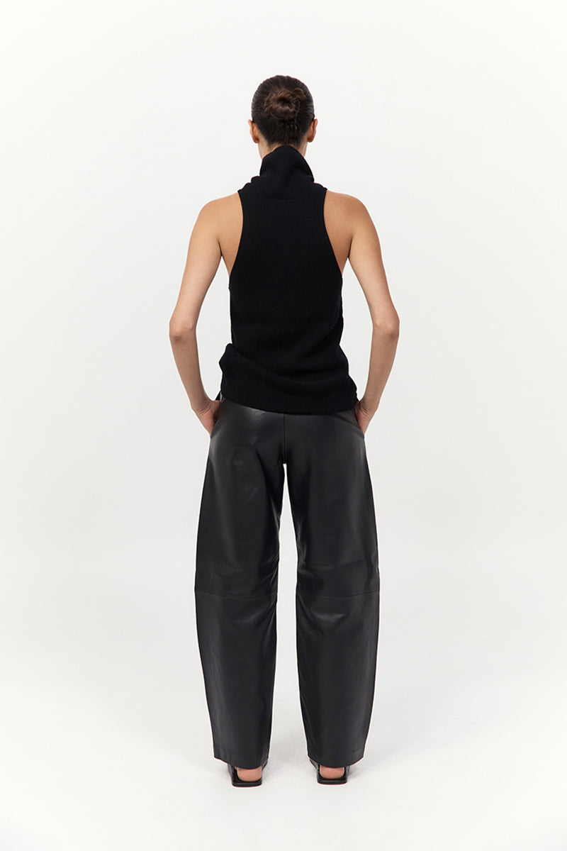 Person wearing a black sleeveless top and leather pants on a white background
