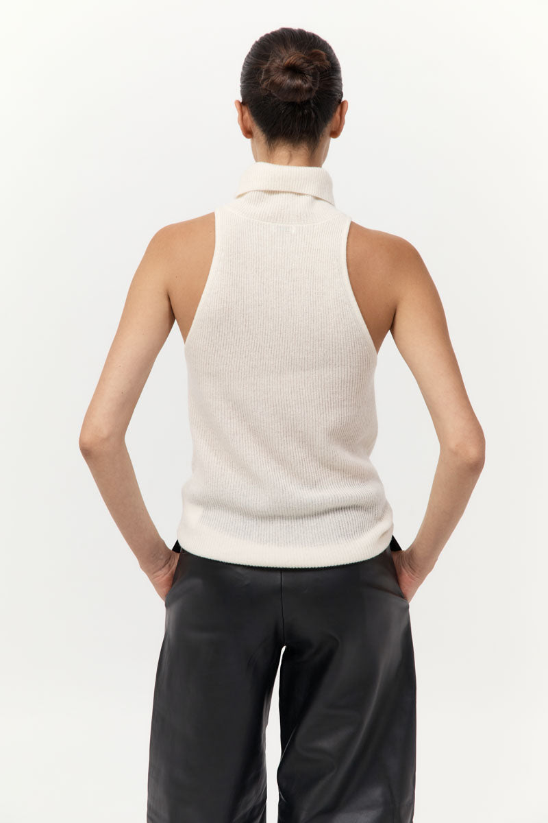 Person wearing a sleeveless cream top and black pants on a white background