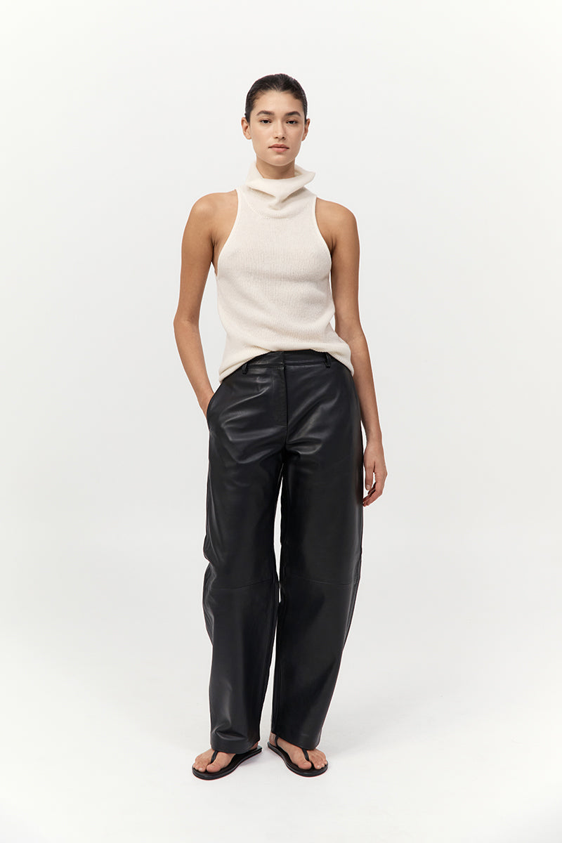 Person wearing a cream sleeveless top and black leather pants on a white background