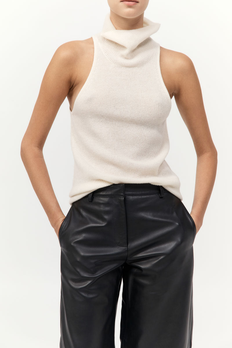 Person wearing a white sleeveless sweater and black leather pants on a plain background