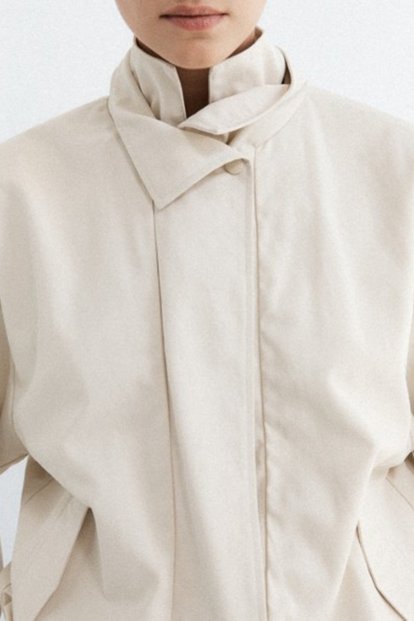 Close-up of a person wearing a beige coat with a plain background