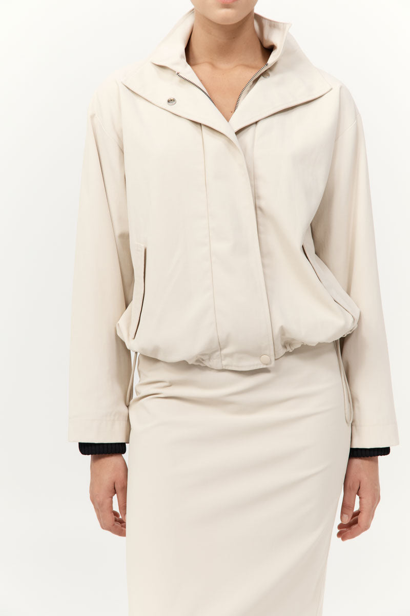 Person wearing a cream-colored outfit with a jacket and skirt on a white background