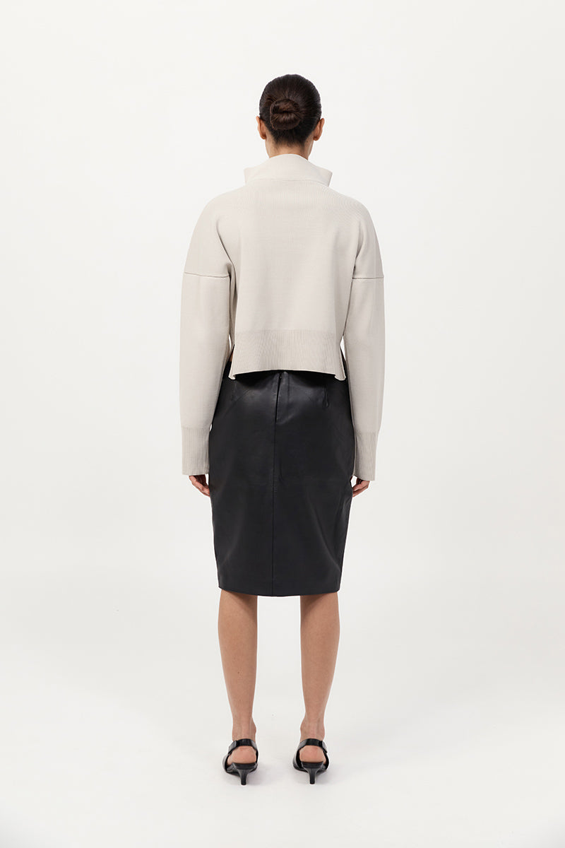 Person wearing a light gray turtleneck and black leather skirt on a white background