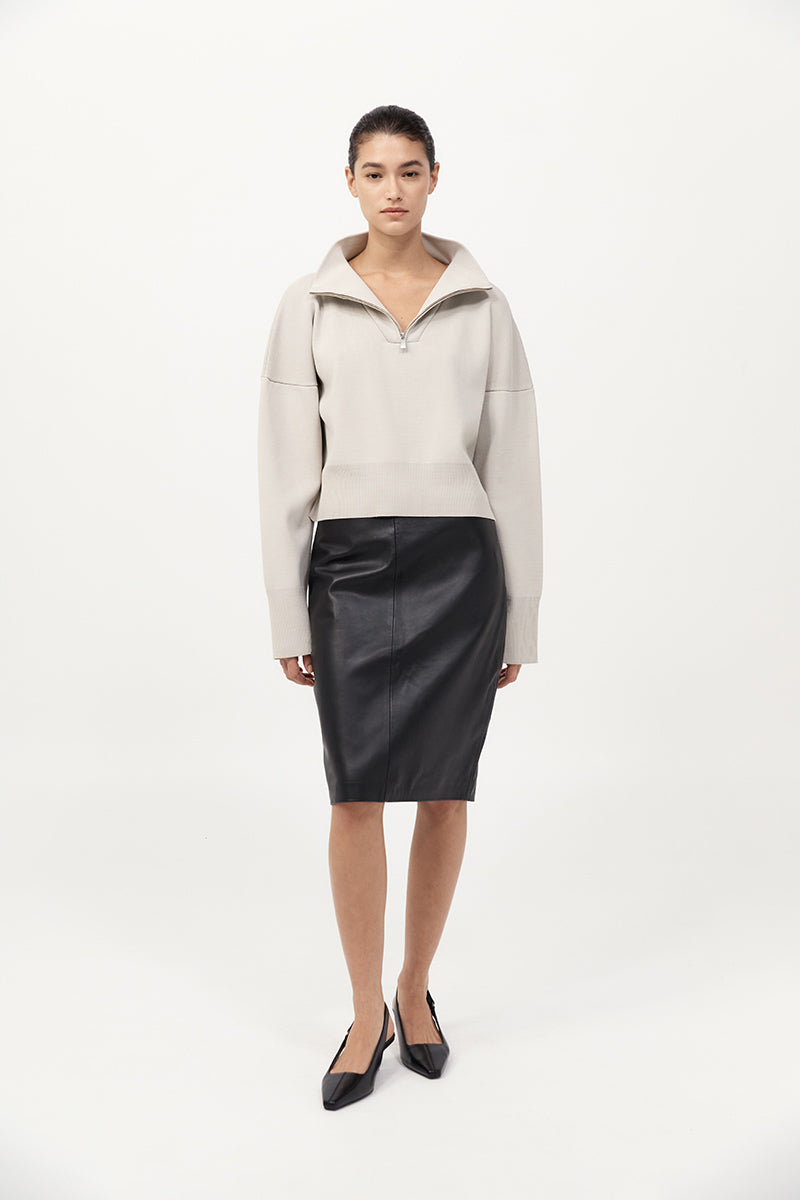 Woman wearing a beige sweater and black skirt on a white background
