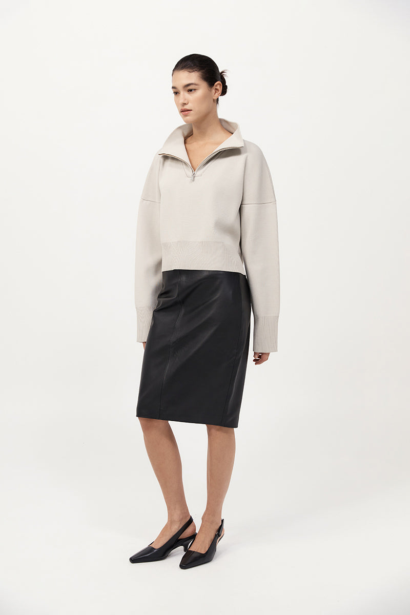 Woman wearing a beige sweater and black skirt on a white background