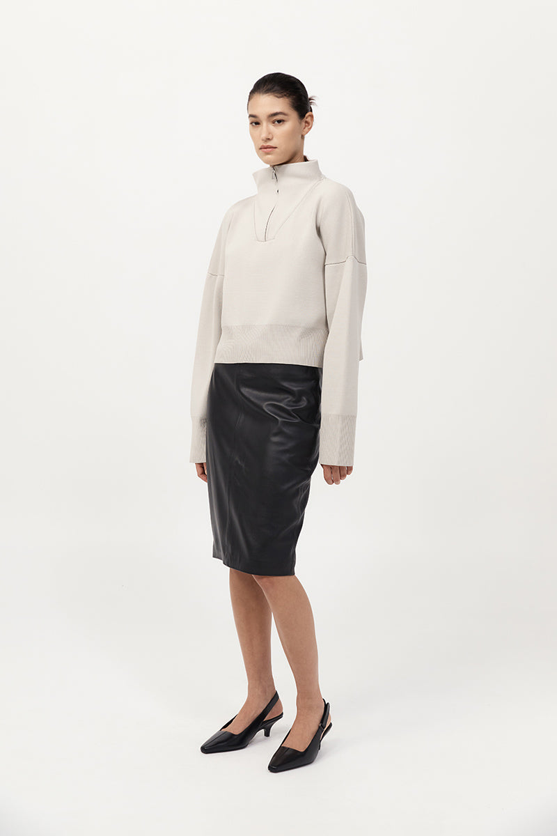 Woman wearing a cream sweater and black leather skirt on a white background