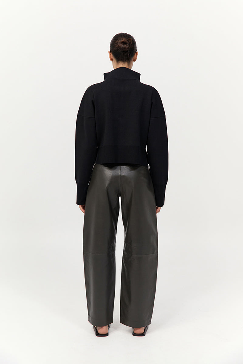 Person wearing a black shirt and gray pants on a white background