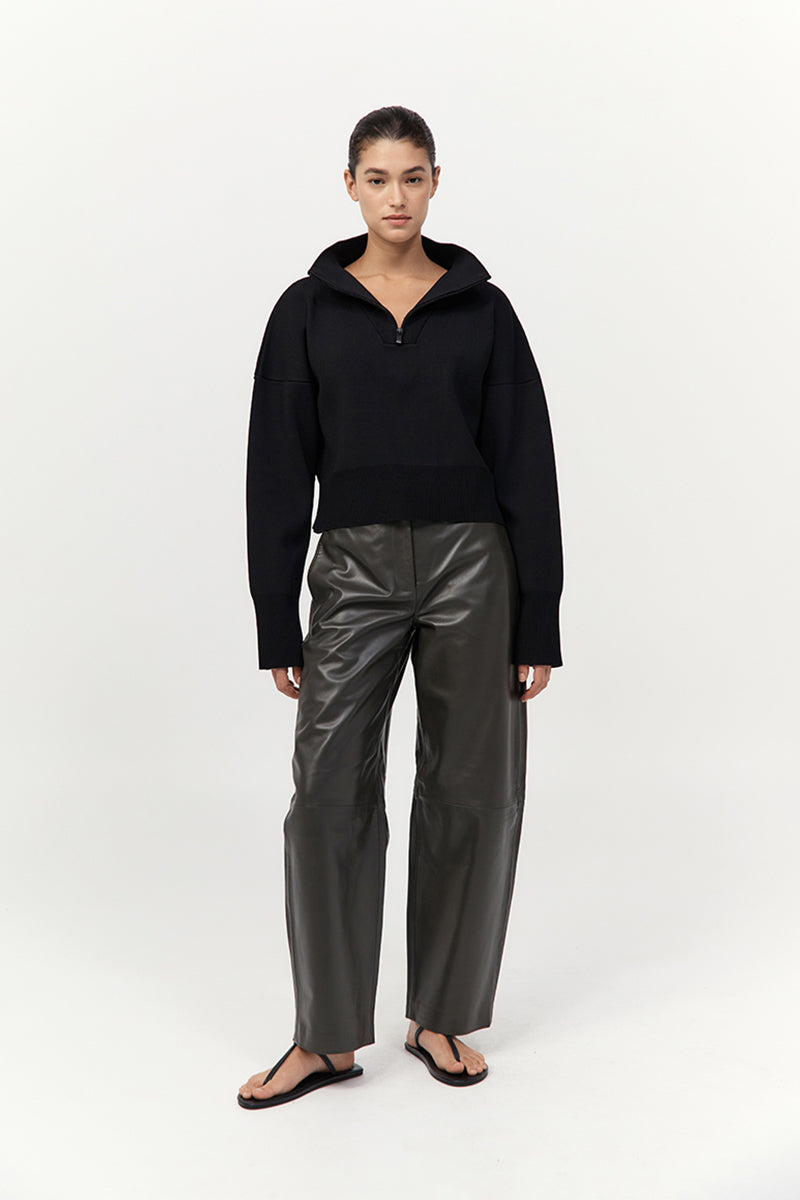 Person wearing a black hoodie and shiny gray pants on a white background