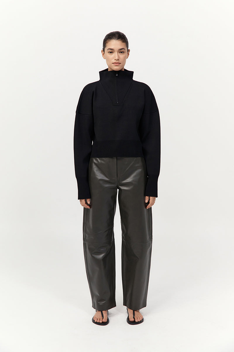 Person wearing a black outfit with a high collar and dark pants on a white background
