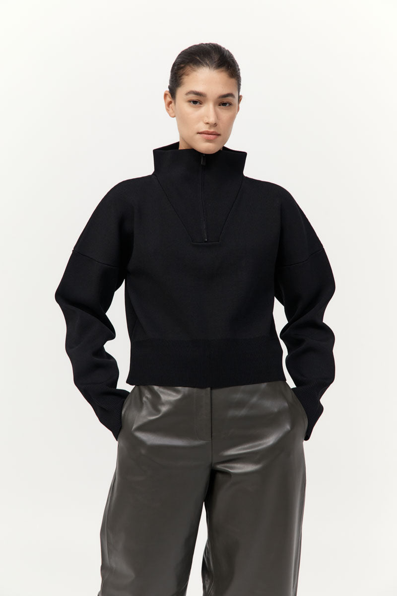 Person wearing a black sweater and gray pants on a white background