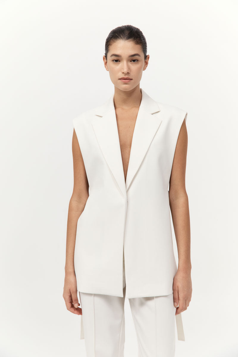 Woman wearing a white sleeveless blazer over a plain background