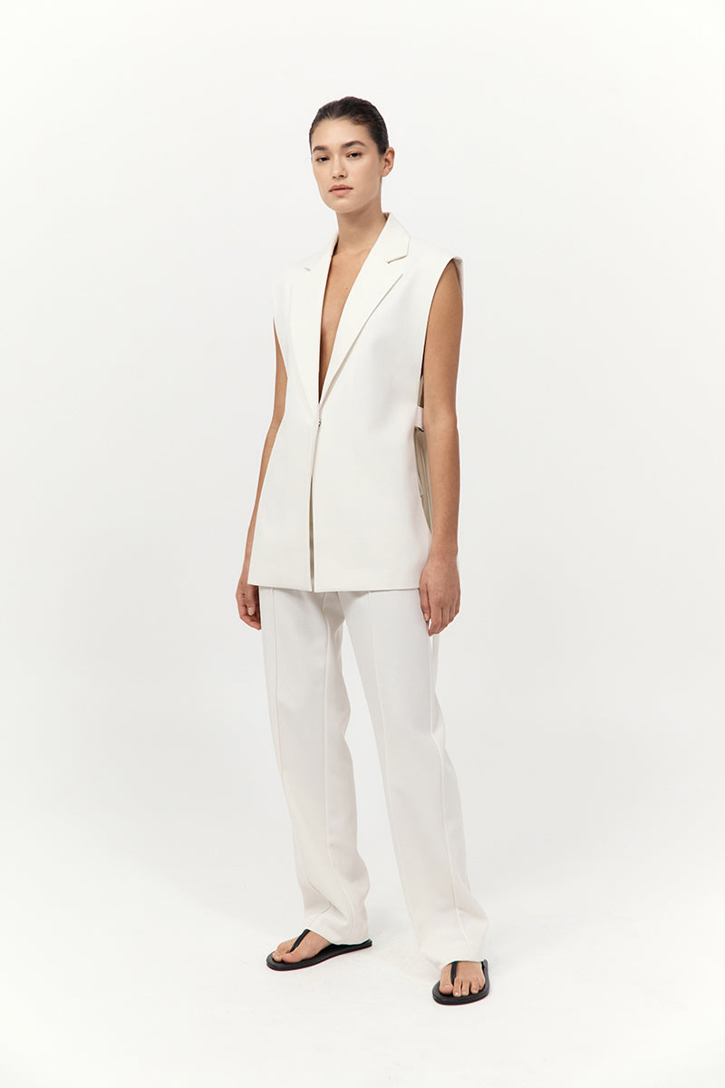 Woman wearing a white sleeveless blazer and pants on a white background