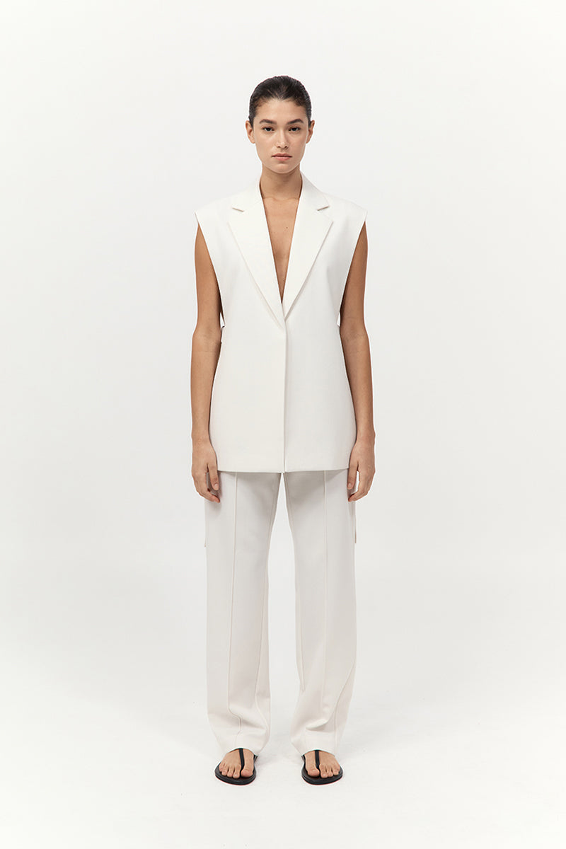 Woman wearing a white sleeveless blazer and pants on a white background