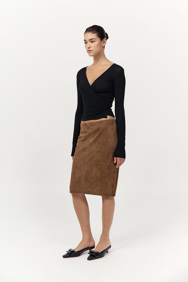 Woman wearing a black long-sleeve top and brown skirt on a white background