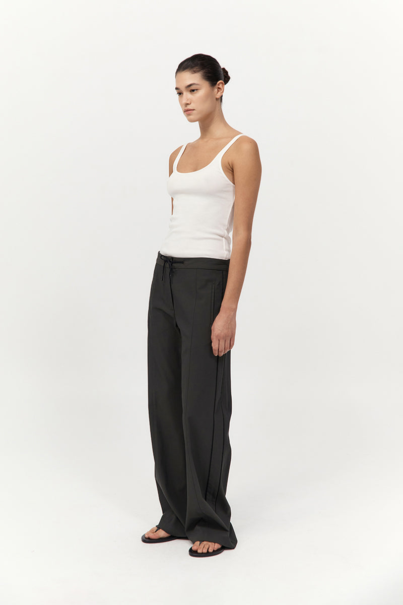 Woman wearing a white tank top and black pants on a white background
