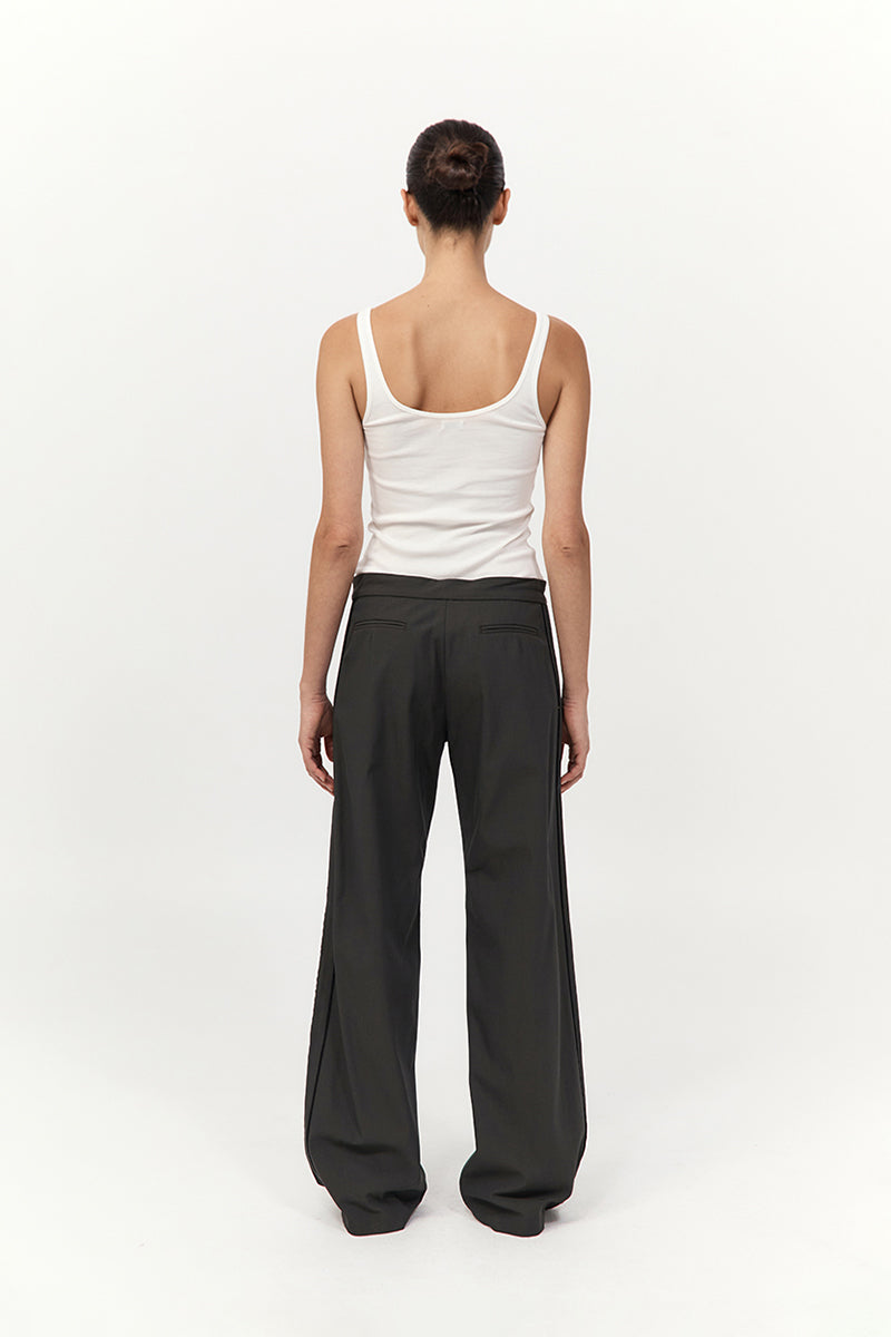 Person wearing a white tank top and dark green pants on a white background