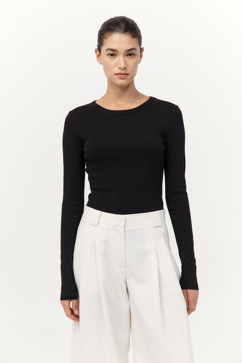 Woman wearing a black long-sleeve top and white pants on a white background