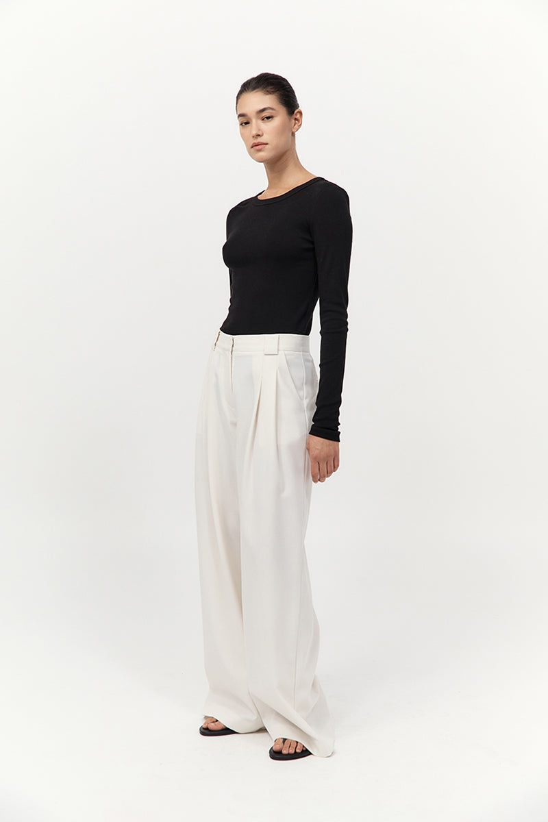 Woman wearing a black top and white pants on a white background
